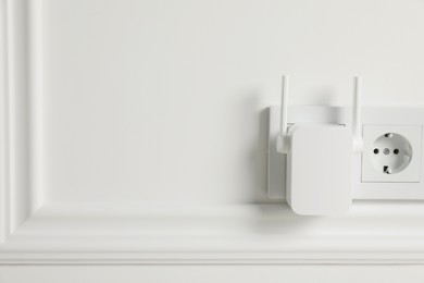 Wireless Wi-Fi repeater on white wall indoors, space for text