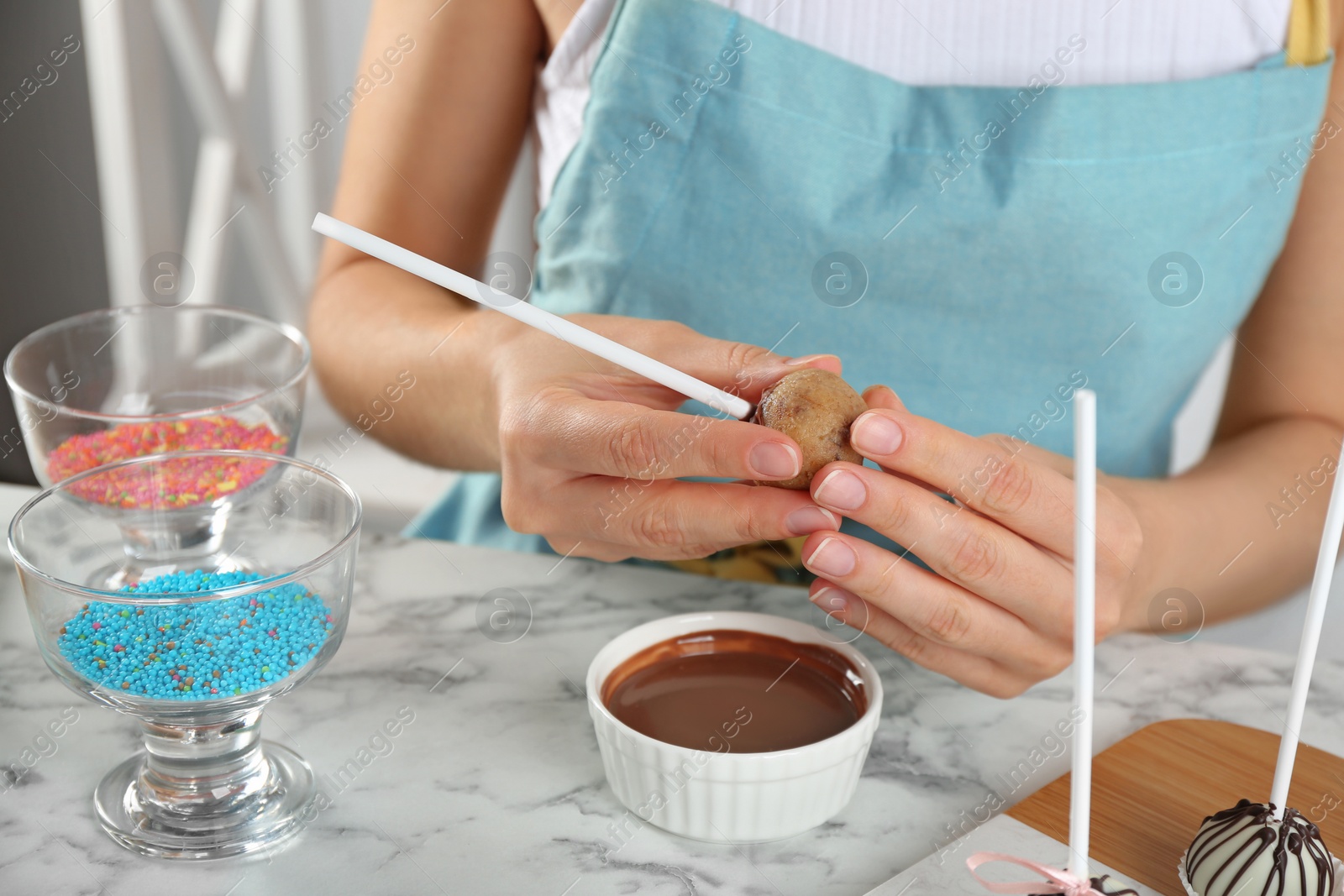 Photo of Young woman with cake pop and chocolate frosting at white marble table, closeup