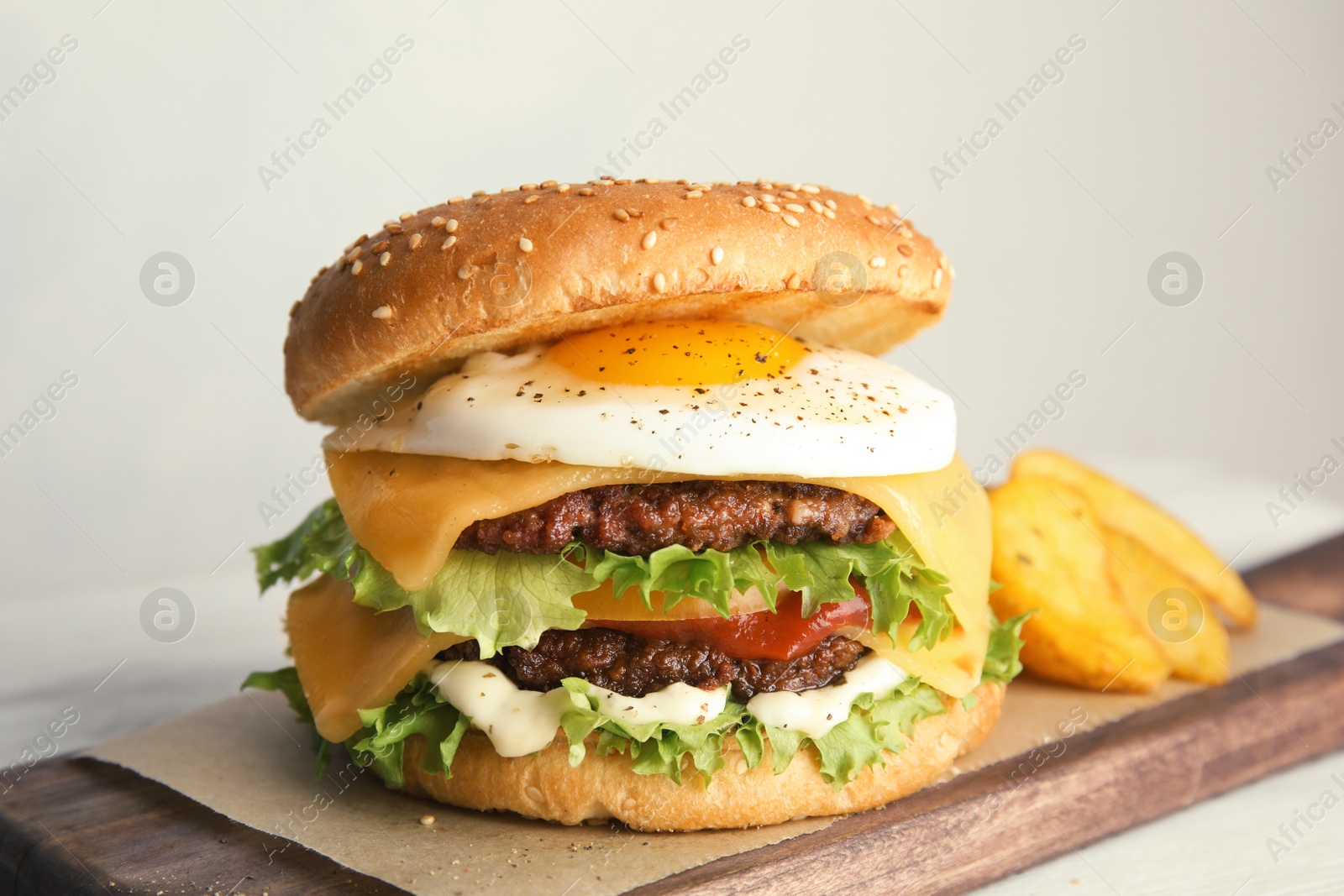 Photo of Tasty burger with fried egg on board against light background