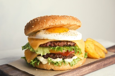 Tasty burger with fried egg on board against light background