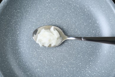 Photo of Organic coconut cooking oil and spoon on frying pan, top view