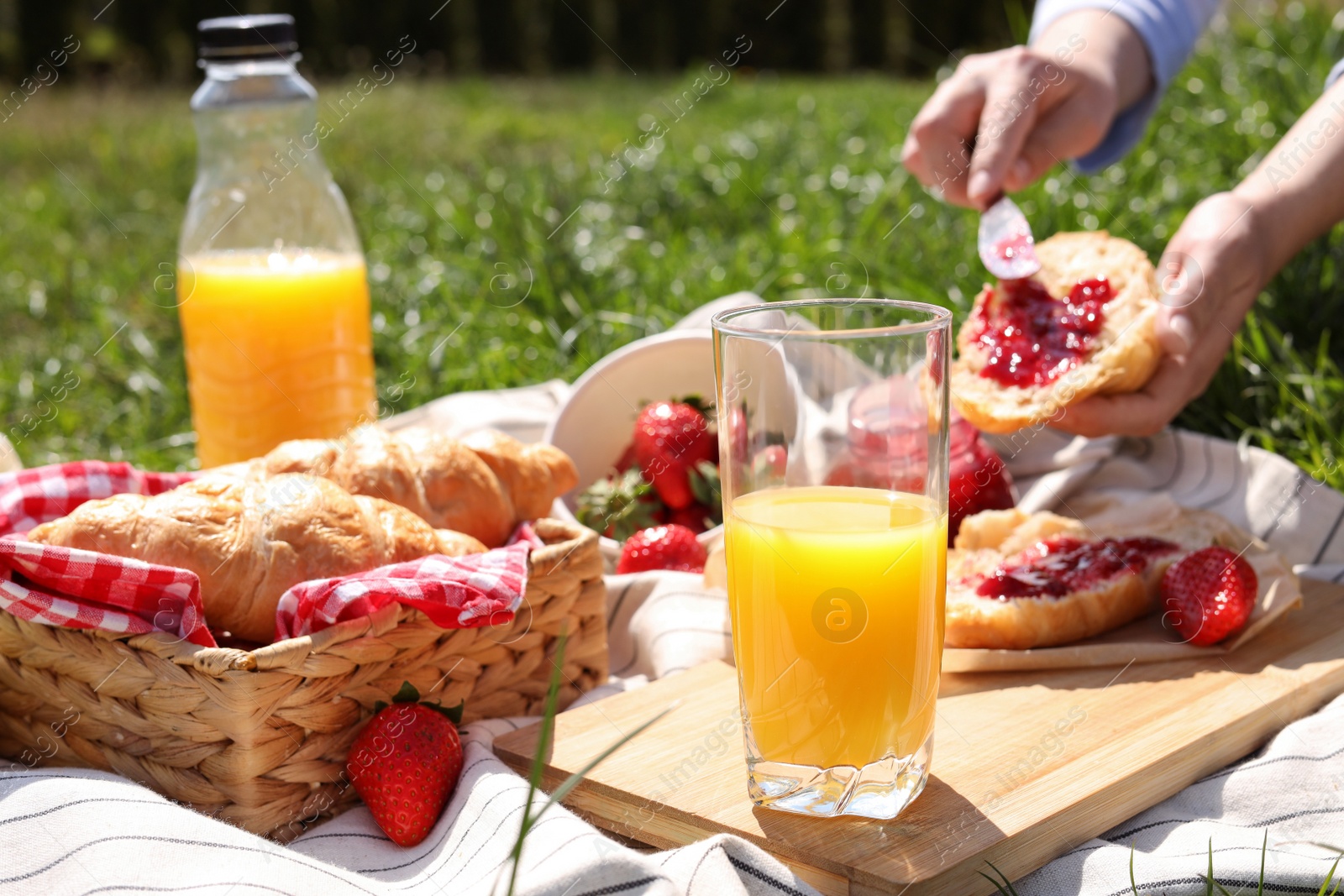 Photo of Woman with croissant outdoors, focus on glass of juice. Summer picnic