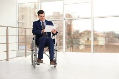 Young businessman in wheelchair using tablet near window indoors