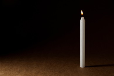 Photo of Burning church wax candle on dark background, space for text