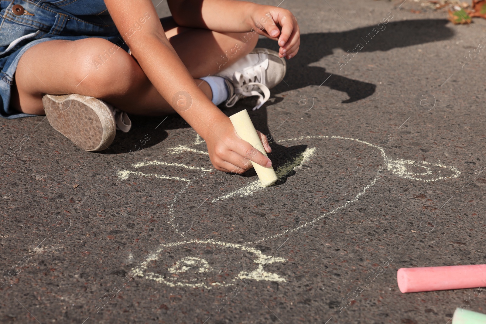 Photo of Little child drawing cat with colorful chalk on asphalt, closeup