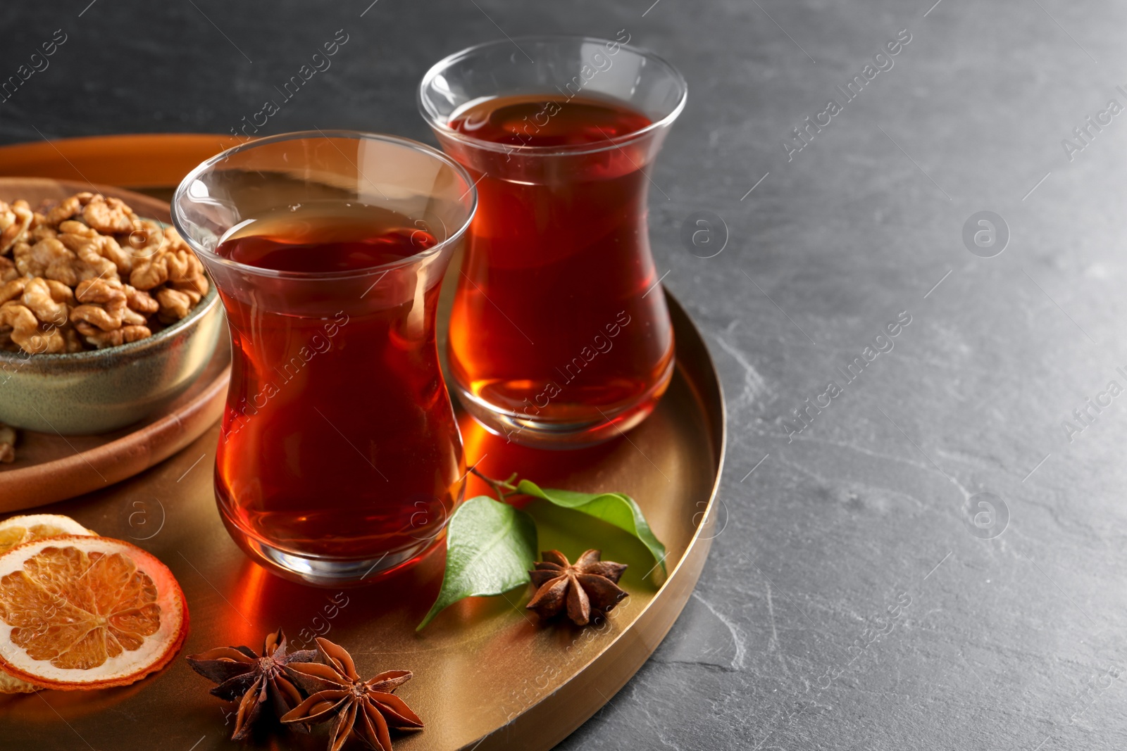 Photo of Tray with glasses of traditional Turkish tea, walnuts, dried orange and anise on black table, closeup. Space for text