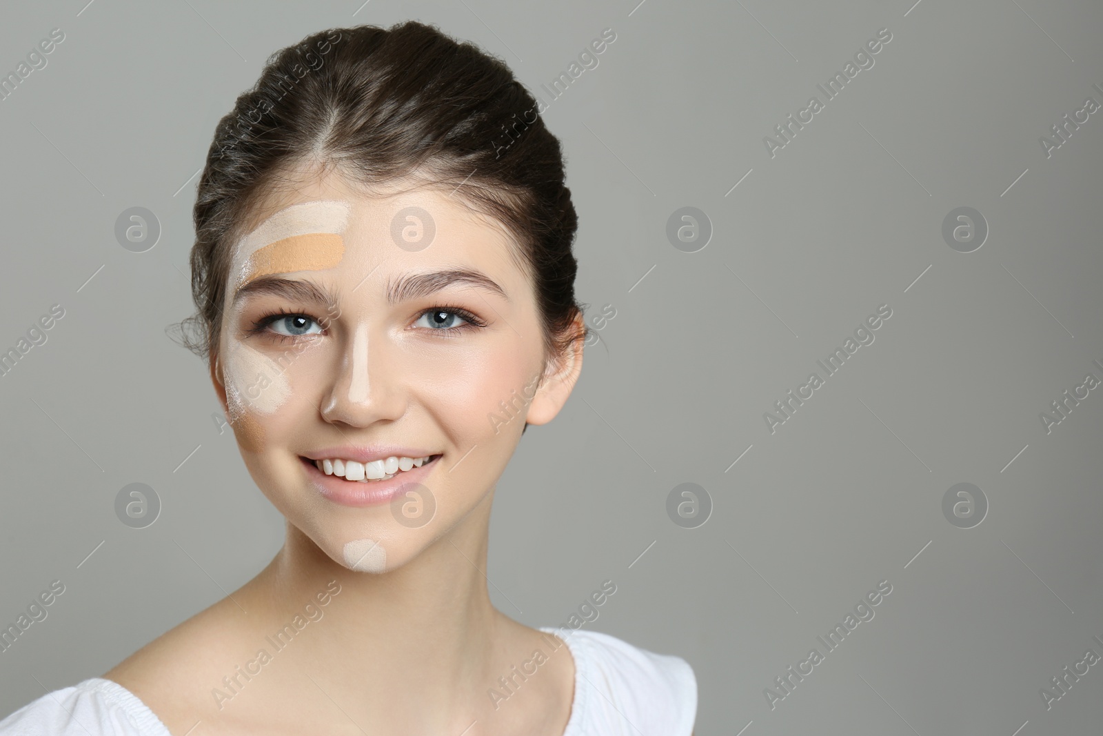 Photo of Beautiful girl on grey background. Using concealers and foundation for face contouring