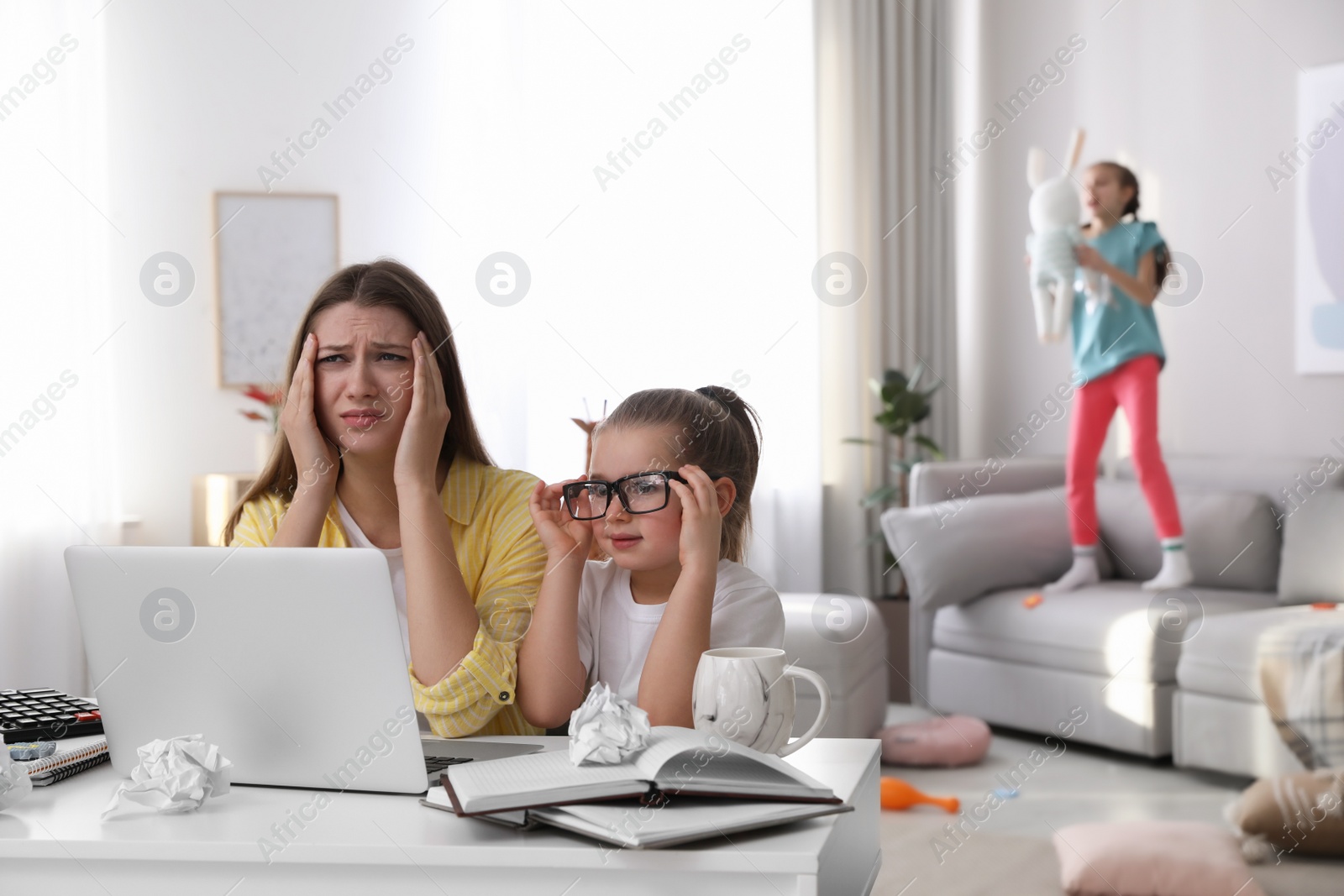 Photo of Children disturbing stressed woman in living room. Working from home during quarantine