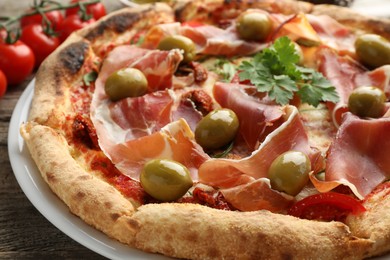 Tasty pizza with cured ham, olives, tomatoes and parsley on wooden table, closeup