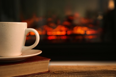 Cup with hot drink and book on table against fireplace, space for text