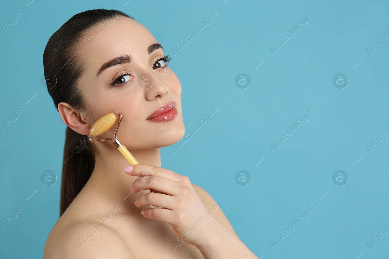 Photo of Woman using natural jade face roller on light blue background, space for text