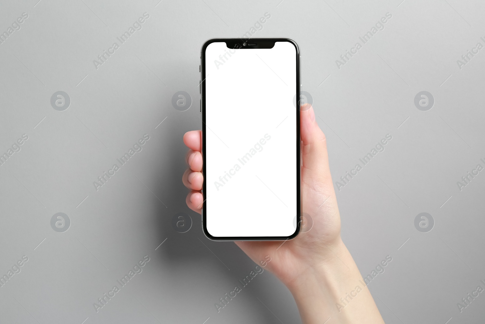 Photo of Woman holding smartphone with blank screen on grey background, closeup. Mockup for design