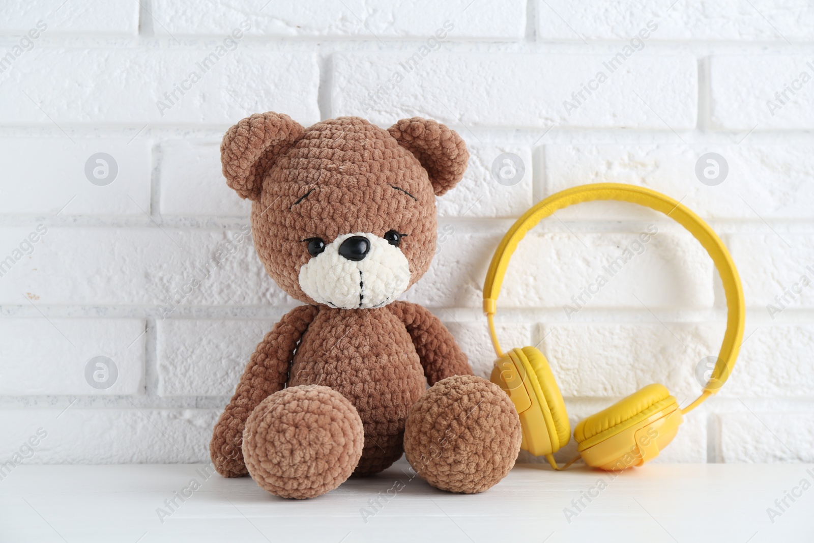 Photo of Baby songs. Toy bear and yellow headphones on white wooden table