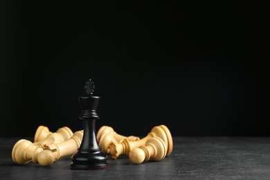 Photo of King among fallen chess pieces on black table against dark background. Space for text