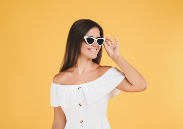 Young woman wearing stylish white dress on yellow background