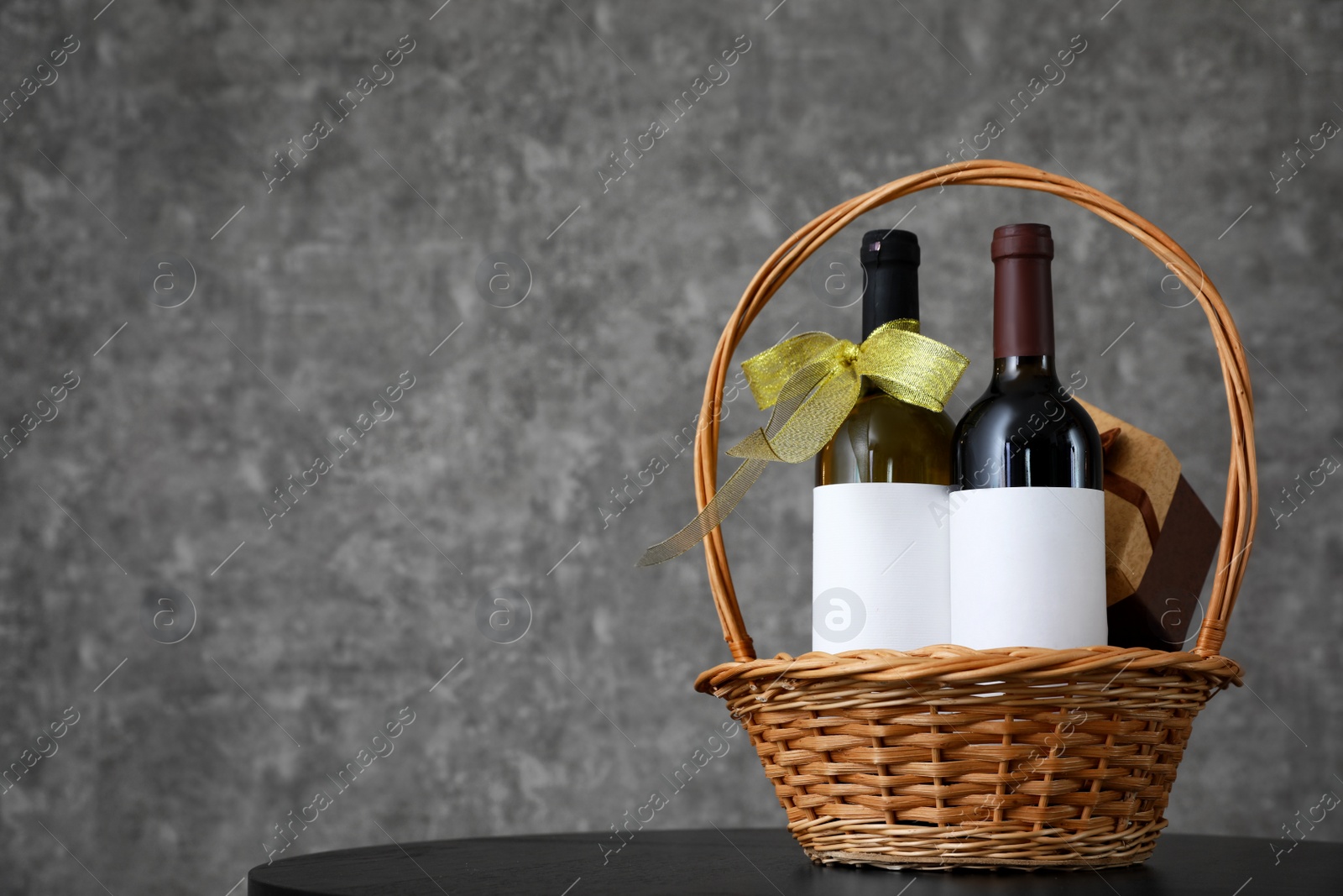 Photo of Wicker basket with bottles of wine and gift box on table. Space for design