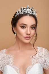 Beautiful young woman wearing luxurious tiara on beige background