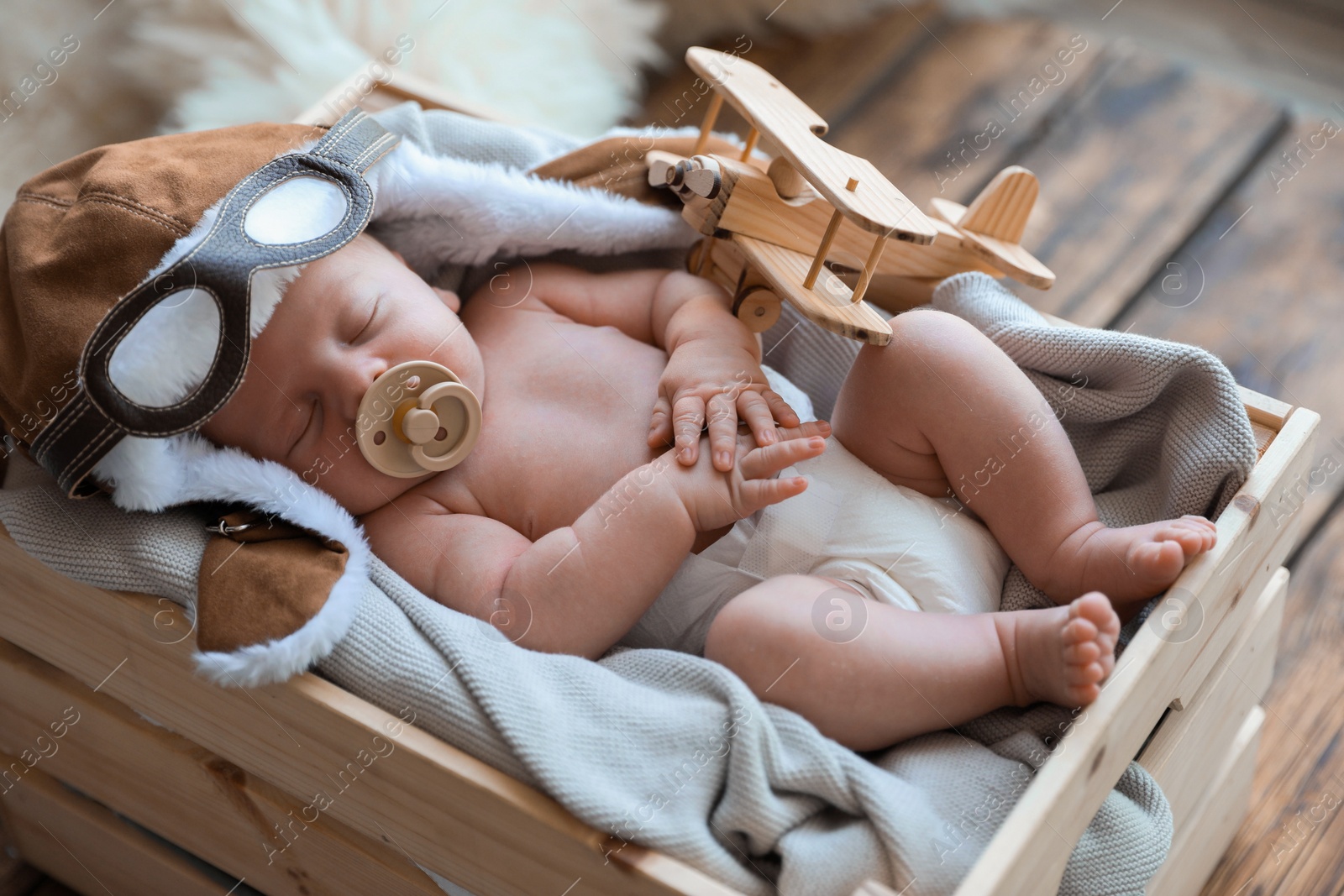 Photo of Cute newborn baby wearing aviator hat with toy sleeping in wooden crate