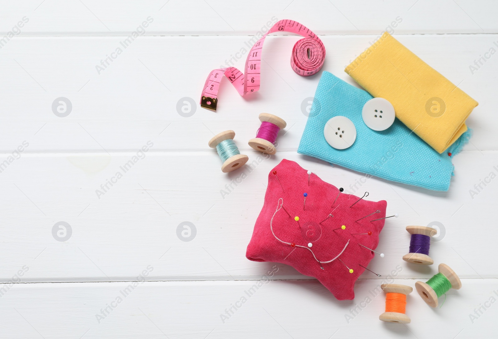 Photo of Red pincushion with pins and other sewing tools on white wooden table, flat lay. Space for text