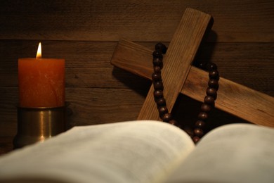 Photo of Church candle, wooden cross, rosary beads and Bible on table