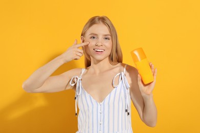 Photo of Beautiful young woman holding sun protection cream on orange background