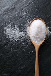 Photo of Organic white salt in spoon on black table, top view. Space for text