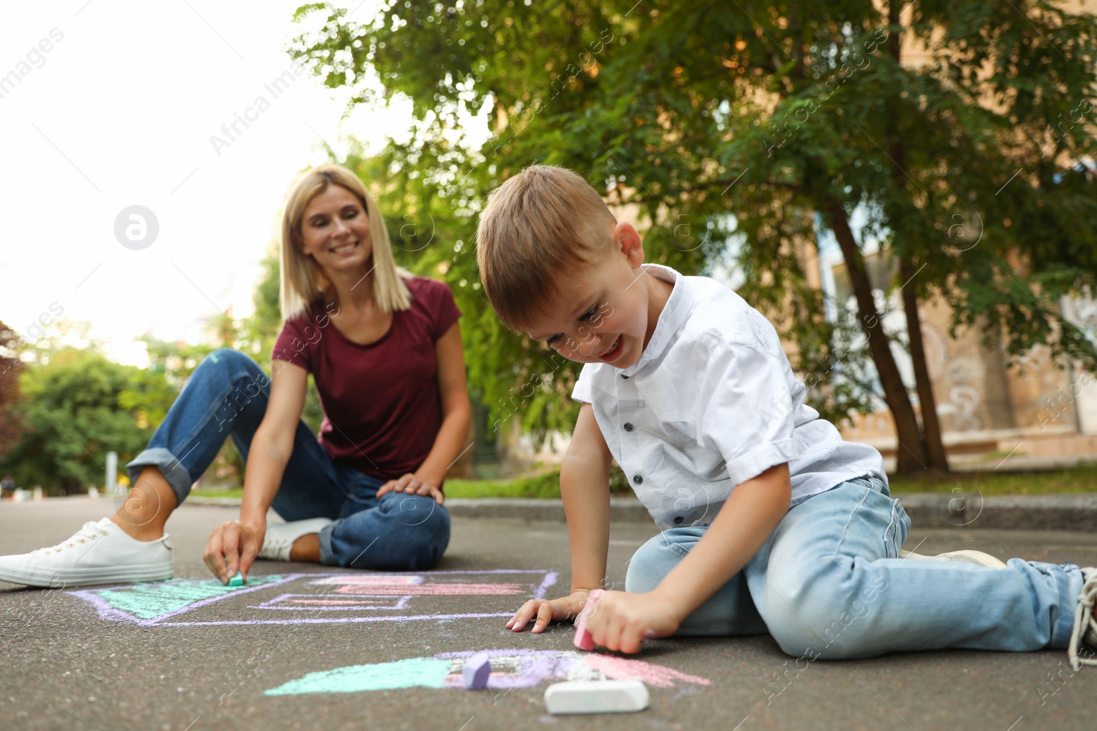 Photo of Nanny with cute little boy drawing house with chalks on asphalt