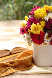 Photo of Vase with beautiful bouquet, open book and cloth on wooden table