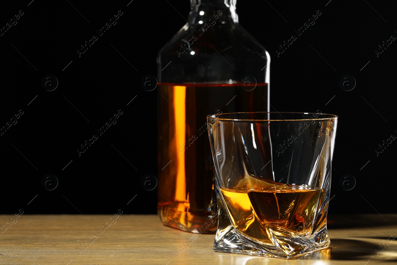 Photo of Whiskey in glass and bottle on wooden table against black background. Space for text