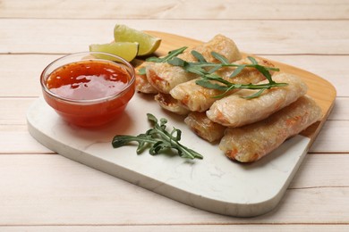 Photo of Tasty fried spring rolls, lime, arugula and sauce on light wooden table, closeup