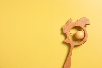 Baby accessories. Wooden rattle on yellow background, top view. Space for text