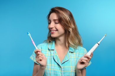 Young woman choosing between manual and electric toothbrushes on color background