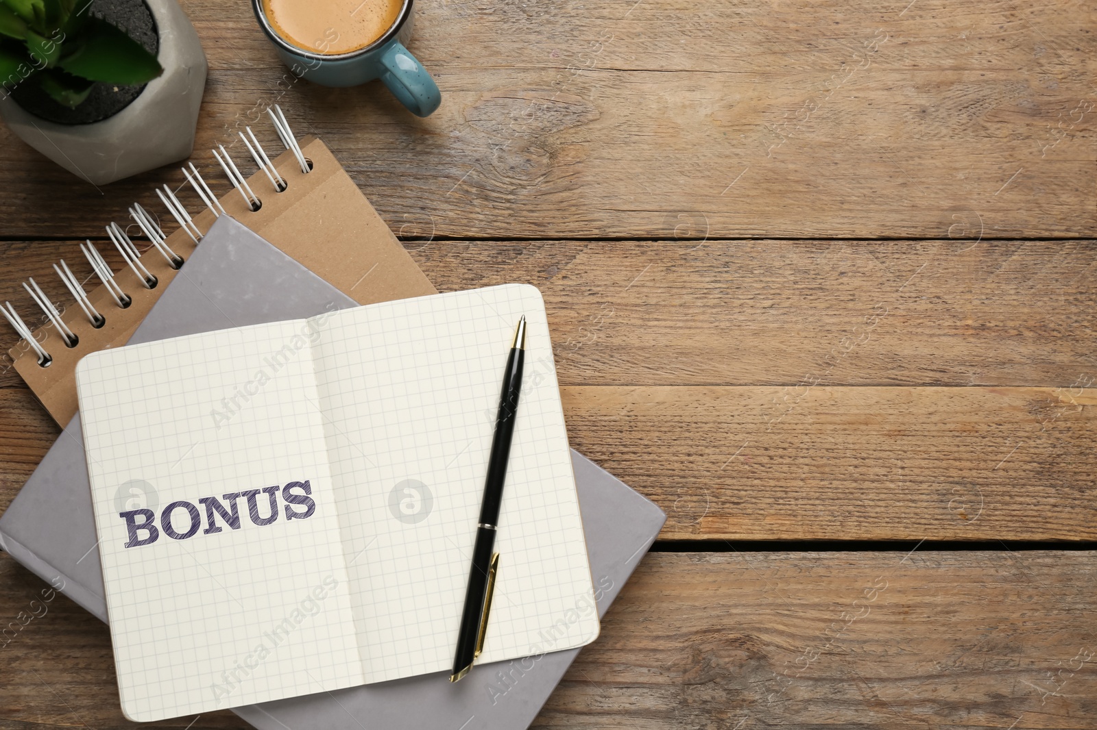 Image of Word Bonus written in notebook, coffee and stationery on wooden table, flat lay