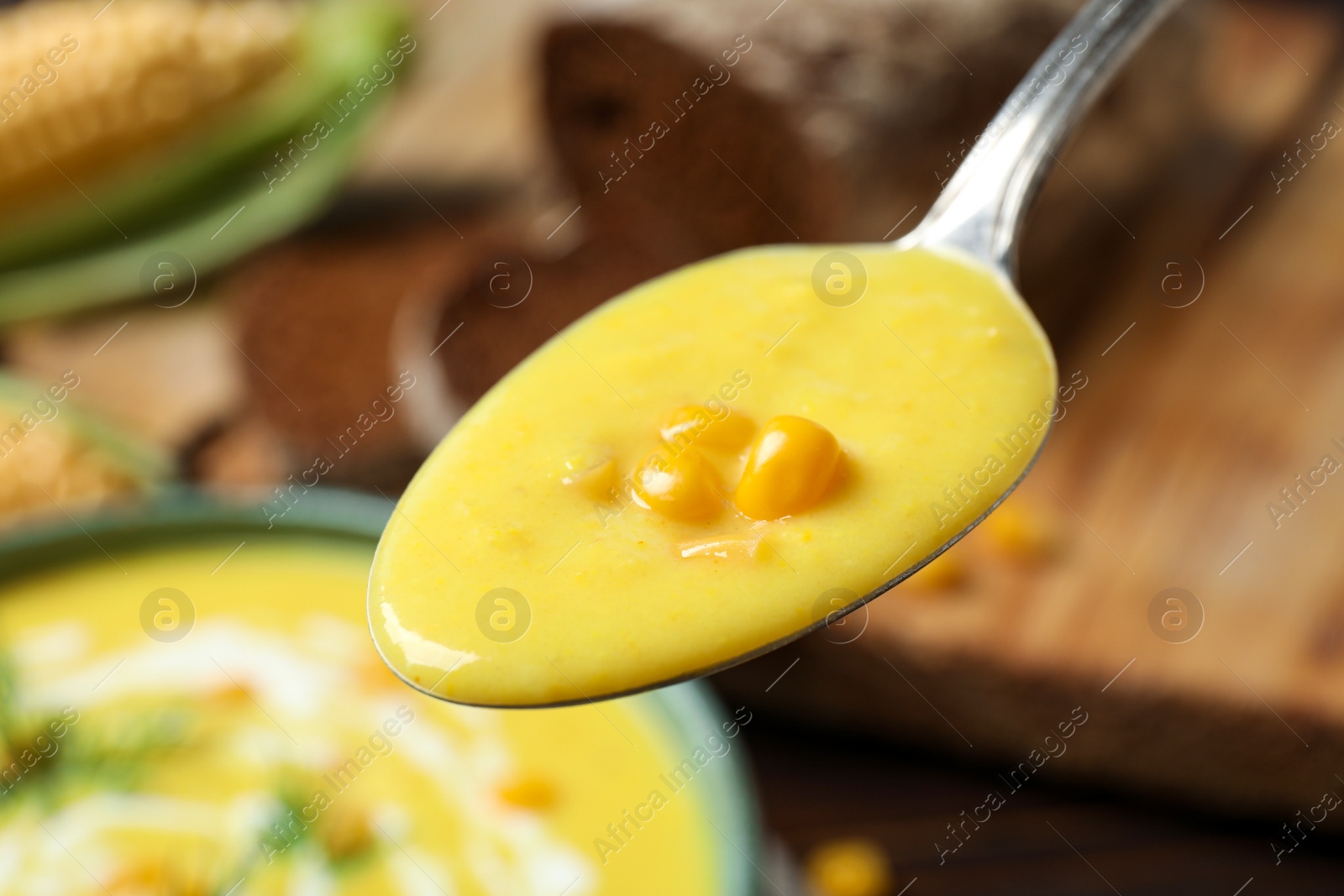 Photo of Spoon of delicious creamy corn soup over bowl, closeup