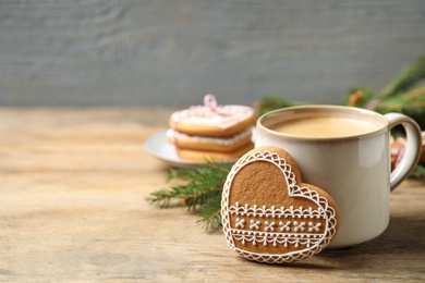 Tasty heart shaped gingerbread cookie and hot drink on wooden table. Space for text