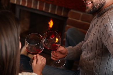 Lovely couple with glasses of wine resting near fireplace at home, closeup. Winter vacation