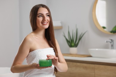 Photo of Young woman holding jar of aloe hair mask in bathroom. Space for text