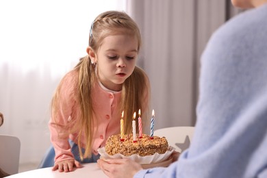 Photo of Birthday celebration. Mother holding tasty cake with burning candles near her daughter indoors