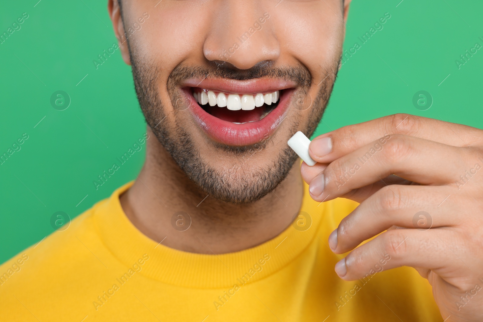 Photo of Happy man putting bubble gum into mouth on green background, closeup