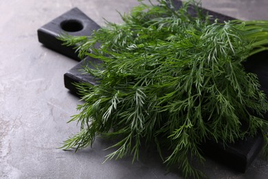 Photo of Board with sprigs of fresh dill on grey textured table, closeup