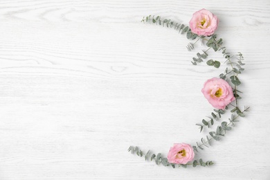 Fresh eucalyptus leaves with flowers and space for design on white wooden background, flat lay