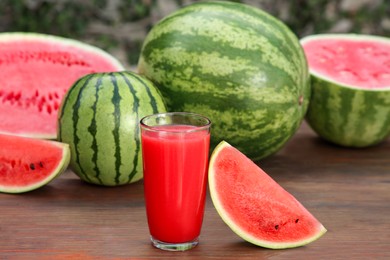 Photo of Delicious ripe watermelons and glass of fresh juice on wooden table outdoors