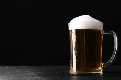 Photo of Cold tasty beer on grey table against dark background. Space for text