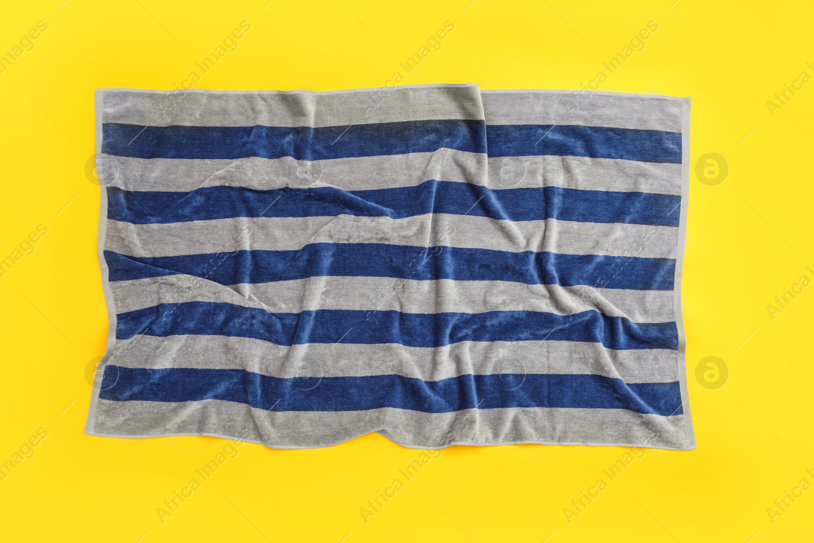 Photo of Crumpled striped beach towel on yellow background, top view