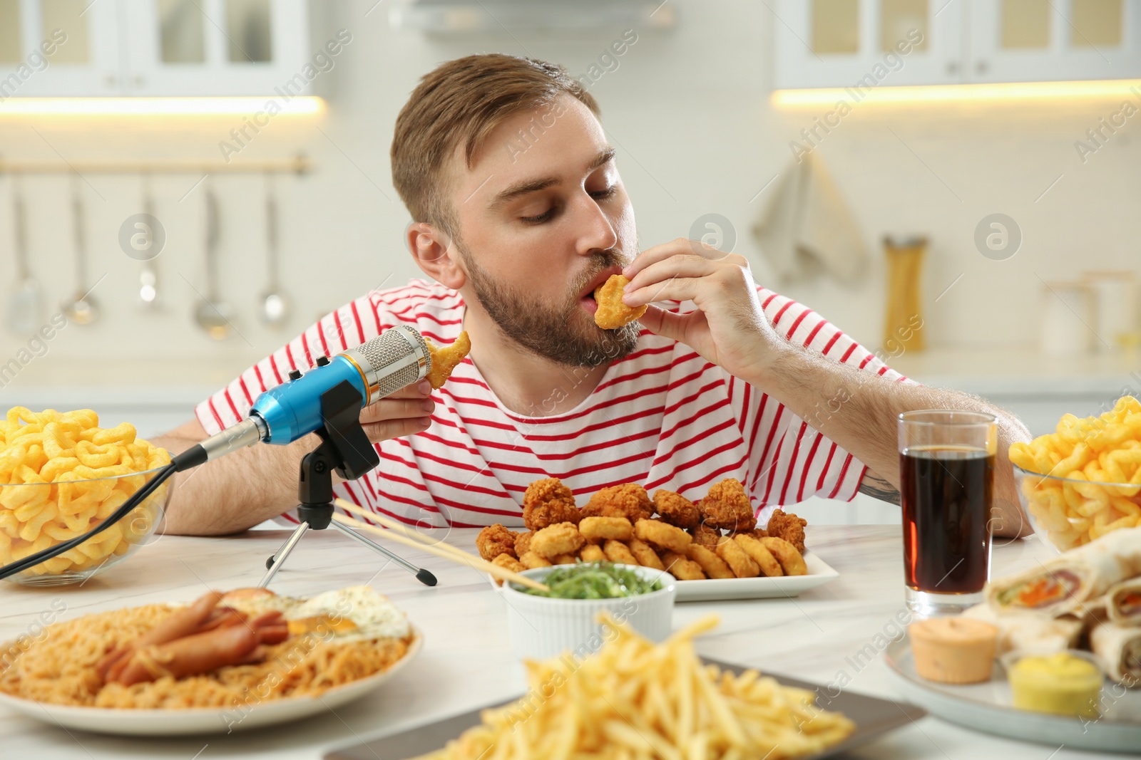 Photo of Food blogger eating near microphone at table in kitchen. Mukbang vlog