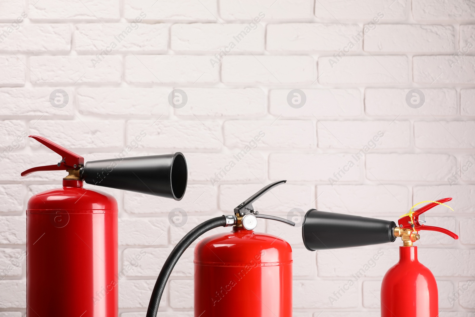 Photo of Fire extinguishers against white brick wall. Space for text