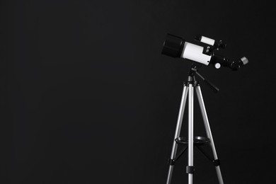 Tripod with modern telescope on black background. Space for text