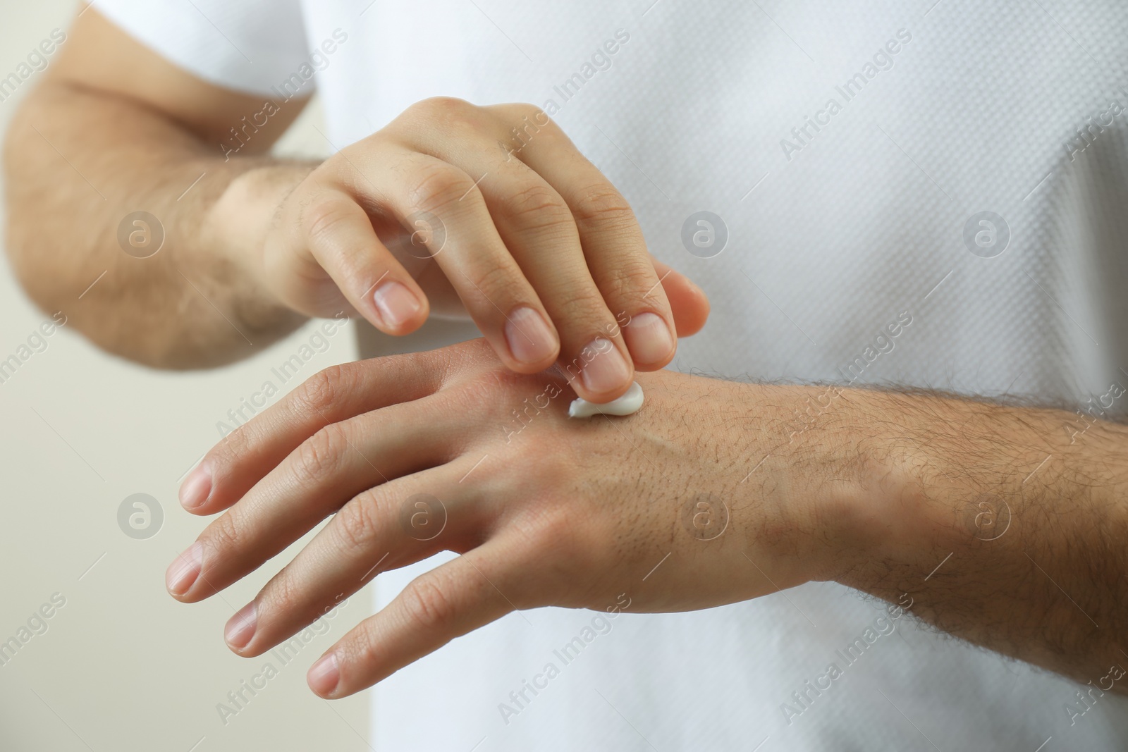 Photo of Man applying cream onto hand on beige background, closeup