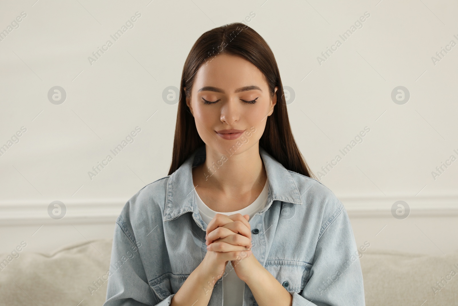 Photo of Religious young woman with clasped hands praying indoors