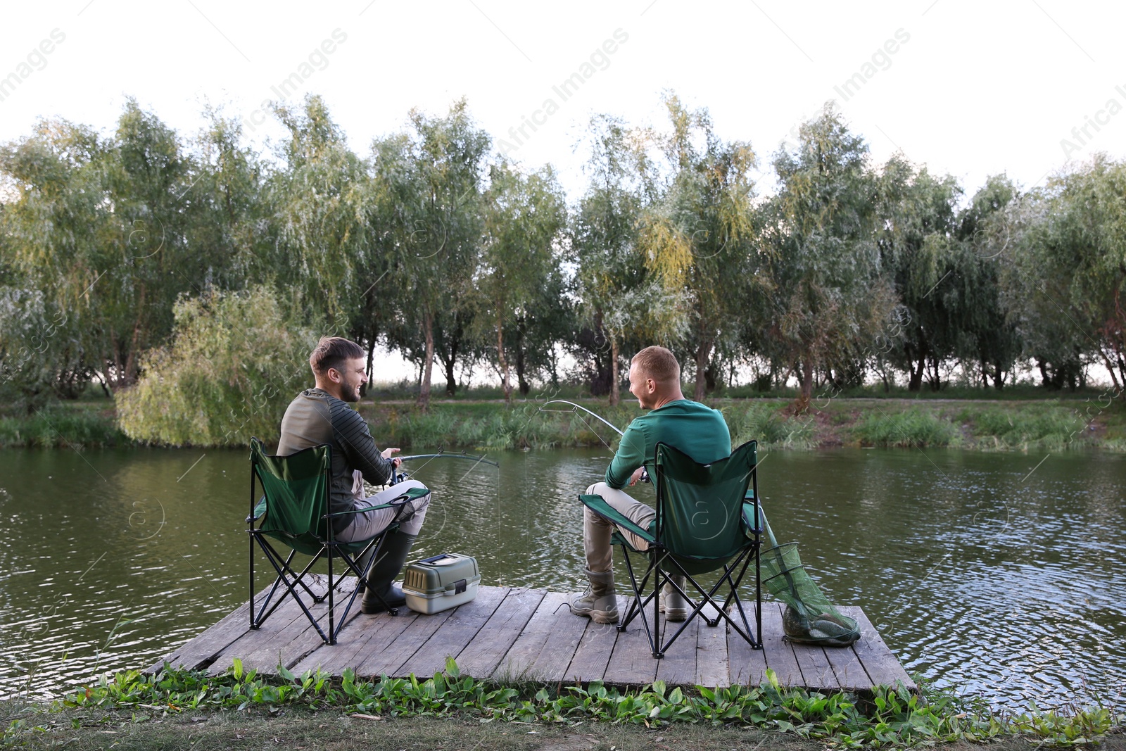 Photo of Friends fishing on wooden pier at riverside. Recreational activity